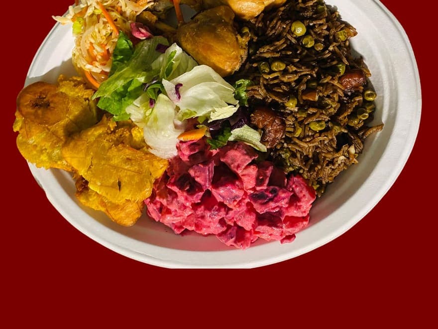 A Haitian plate of fried plantains, pikliz, beetroot salad, legim and rice.